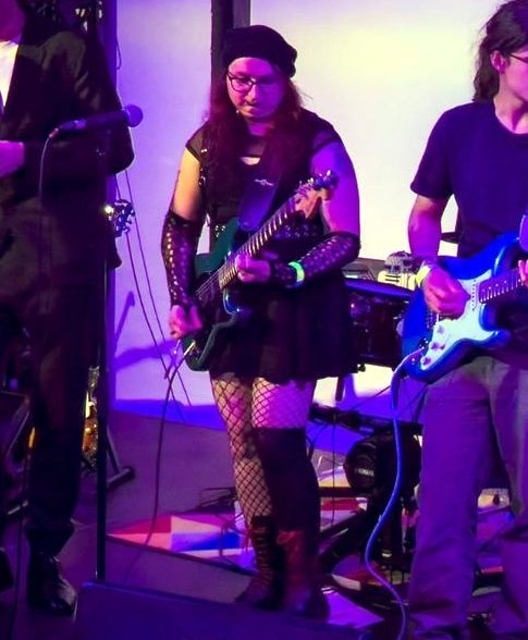 Aya playing a guitar on a stage with blue lighting